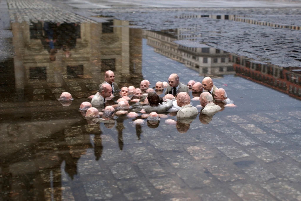 Photo shows an artwork containing small figures representing politicians who are in a puddle, depicting how, as they continue to talk, the water level rises around them, representing rising sea levels due to climate change.