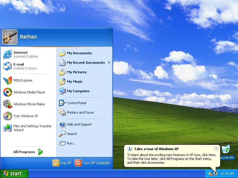 Windows XP, showing an open Start menu, the famous Rolling Green Hills desktop wallpaper, and a tooltip popping up from the taskbar advising us to take a tour of Windows XP. Screenshot.