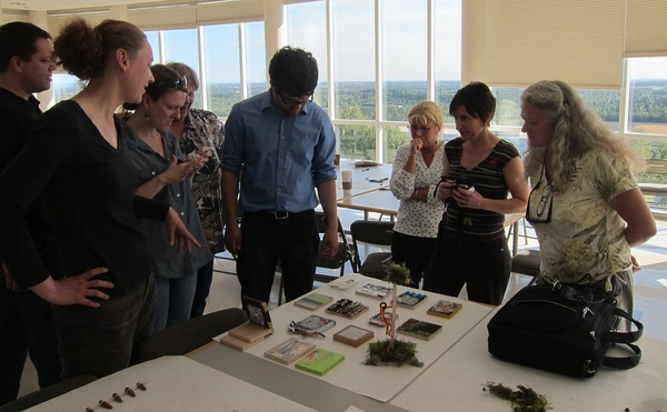 A group of people stand around a table with various office supplies and photos, discussing what they will do next