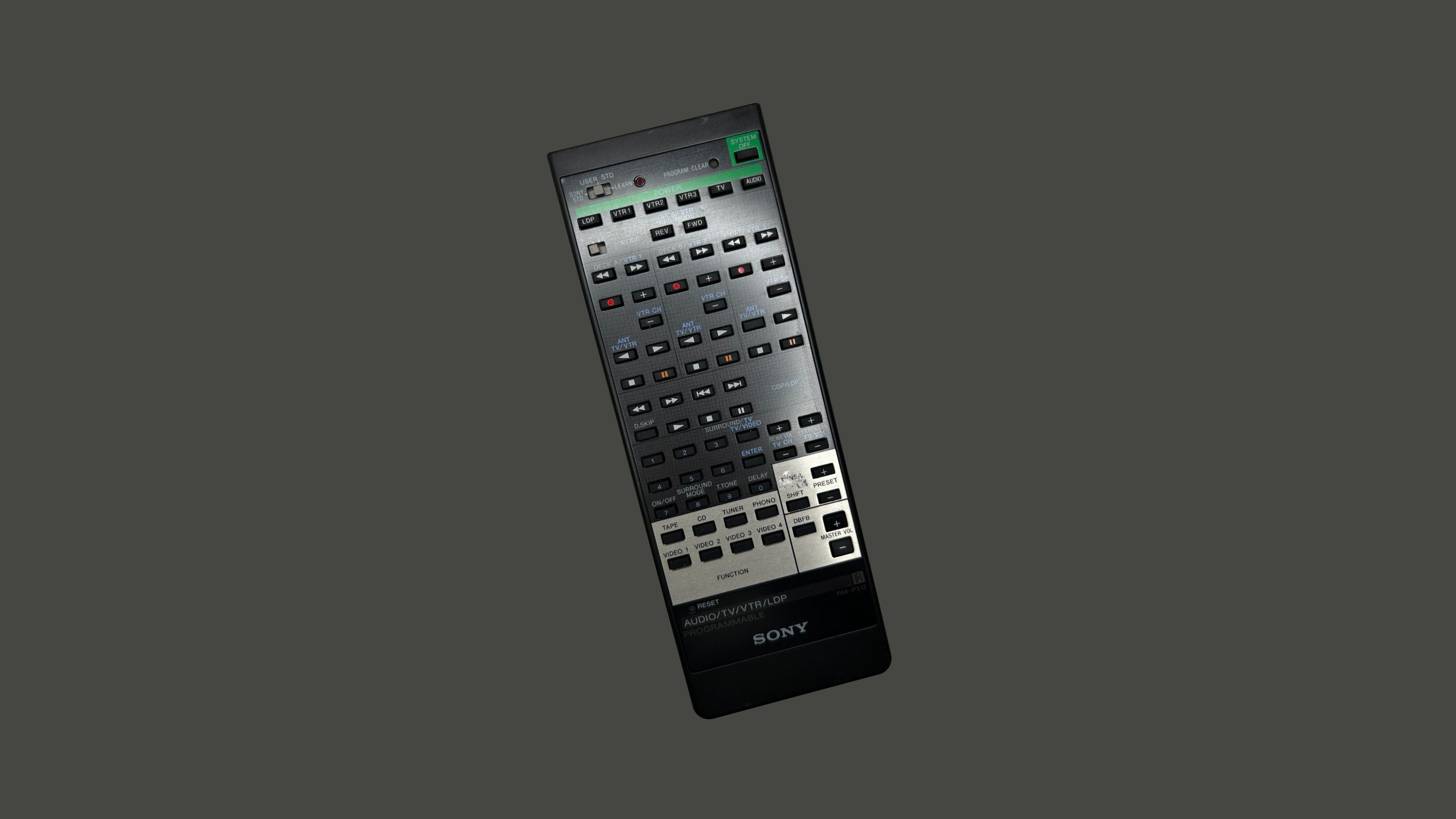 A Sony universal remote control with a metallic faceplate and a black body. It features a large number of small, uniform buttons, all the same shape and size, arranged in a dense grid. The buttons are labeled for various functions, including playback controls, numeric input, and device selection. This design allows the remote to control multiple devices, consolidating numerous functions into a single unit but means that the remote will have a significantly larger number of buttons than a standard TV remote.